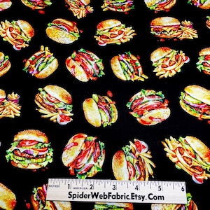 May include: A black fabric featuring a repeating pattern of cheeseburgers and french fries. A white ruler is positioned at the bottom, showing measurements in inches, with the text SpiderWebFabric.Etsy.com printed clearly on the ruler surface.