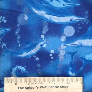 May include: Blue fabric with a repeating pattern of dolphins swimming in a blue ocean with white bubbles. The fabric is measured with a ruler that reads "The Spider's Web Fabric Shop".