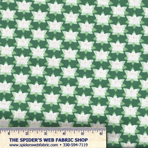 Op de afbeelding: Groene stof met een herhalend patroon van witte en lichtgroene gestileerde bloemen. De bloemen hebben een geel detail in het midden. De stof heeft een liniaal langs de onderrand met de tekst "THE SPIDER'S WEB FABRIC SHOP".