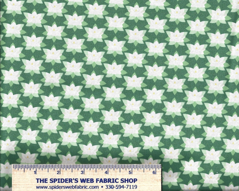 Op de afbeelding: Groene stof met een herhalend patroon van witte en lichtgroene gestileerde bloemen. De bloemen hebben een geel detail in het midden. De stof heeft een liniaal langs de onderrand met de tekst "THE SPIDER'S WEB FABRIC SHOP".