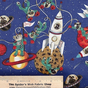 Könnte beinhalten: Blauer Stoff mit einem sich wiederholenden Muster von Cartoon-Hunden in Raumanzügen. Die Hunde fliegen in Raketen, reiten auf Planeten und schweben im Weltraum. Der Stoff hat ein weißes Lineal mit dem Text "The Spider's Web Fabric Shop" und "www.thespiderswebfabricshop.com".