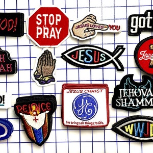Op de afbeelding: Een verzameling van 13 strijkbare patches met christelijke thema's. De patches hebben verschillende ontwerpen, waaronder een vis met het woord "JESUS" erin, een kruis met de woorden "Jezus Christus" en een duif met de woorden "Jehovah Shammah".