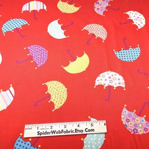 May include: Red fabric with a repeating pattern of colorful umbrellas. The umbrellas have various designs, including stripes, polka dots, and floral patterns. The handles are purple, and the fabric has a ruler at the bottom with the text "SpiderWebFabric.Etsy.com".