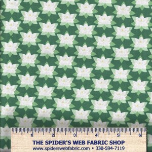 Op de afbeelding: Groene stof met een herhalend patroon van witte lotusbloemen met gele centra en groene bladeren. Langs de onderkant een liniaal met de tekst "THE SPIDER'S WEB FABRIC SHOP".