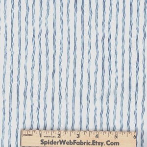 May include: A white fabric featuring a pattern of vertical, wavy blue stripes. A wooden ruler is positioned at the bottom, showing a scale of 6 inches with the text SpiderWebFabric.Etsy.Com printed clearly on the surface of the ruler.