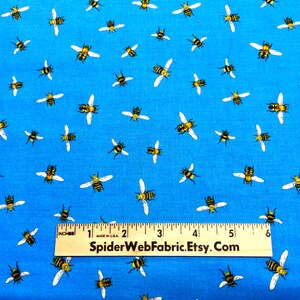 May include: Blue fabric with a repeating pattern of yellow and black bees with white wings. A ruler is placed across the bottom of the fabric. The text "SpiderWebFabric.Etsy.com" is printed on the ruler.