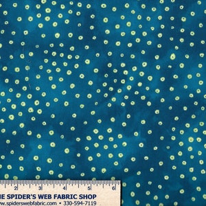 Op de afbeelding: Teal stof met een wit stippenpatroon. De stof heeft een subtiel tie-dye effect. De stof wordt gemeten met een liniaal waarop "The Spider's Web Fabric Shop" en een websiteadres staat.