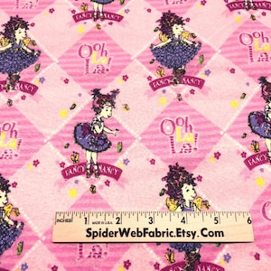 Puede incluir: Tela rosa con un patrón repetido de una niña de dibujos animados con un vestido morado, mariposas y los textos "Fancy Nancy" y "Ooh La La!". El diseño está sobre una cuadrícula de diamantes rosas.