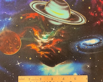 May include: A black fabric with a colorful space scene print. The print features a large planet with rings, a smaller planet, a galaxy, and stars. The fabric is 6 inches wide and has the text "SpiderWebFabric.Etsy.Com" printed on it.