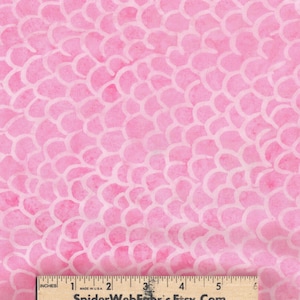 May include: Pink fabric with a repeating pattern of white, petal-like shapes. The fabric has a watercolor effect, with variations in the pink hue. A wooden ruler is at the bottom, showing inches.