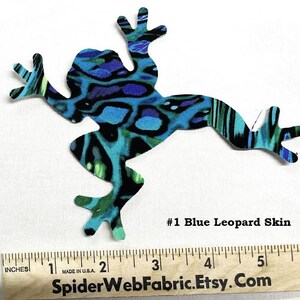 May include: A frog-shaped fabric cutout with a blue leopard skin pattern. The fabric is a mix of blue, black, and green. The text "#1 Blue Leopard Skin" is visible. A wooden ruler with inch measurements is at the bottom.