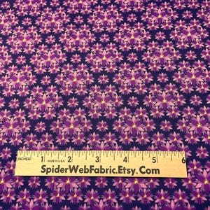 Pode incluir: Tecido com um padrão floral repetitivo em tons de roxo e rosa sobre um fundo azul escuro. Uma régua com polegadas é colocada sobre o tecido. O texto "SpiderWebFabric.Etsy.Com" está impresso na régua.
