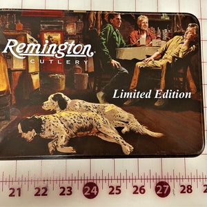 May include: A vintage-style tin box with a scene of three men sitting around a table with two dogs in the foreground. The box features the Remington Cutlery logo and the text "Limited Edition".