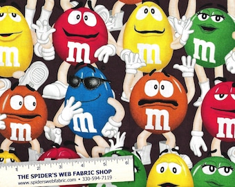 May include: A colorful fabric featuring a repeating pattern of M&M's characters. The characters are wearing white gloves and shoes. The background is a dark brown color. The text "THE SPIDER'S WEB FABRIC SHOP" and "www.spiderswebfabric.com 330-594-7119" is printed at the bottom of the fabric.
