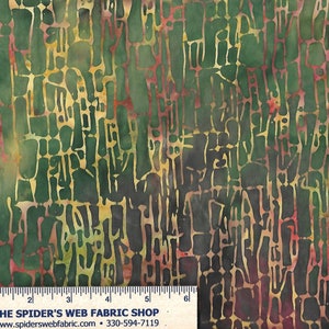 May include: Green, brown, and red batik fabric with a repeating pattern of abstract shapes. The fabric is shown with a ruler for scale.