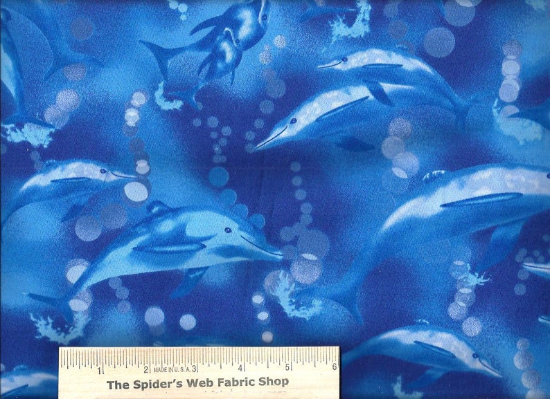 May include: Blue fabric with a repeating pattern of dolphins swimming in a blue ocean with white bubbles. The fabric has a ruler with the text "The Spider's Web Fabric Shop" printed on it.