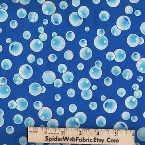 May include: A blue fabric featuring a repeating pattern of light blue and white bubbles of varying sizes. A wooden ruler is positioned at the bottom, showing a measurement scale of 5 inches with the text SpiderWebFabric.Etsy.Com printed on it.