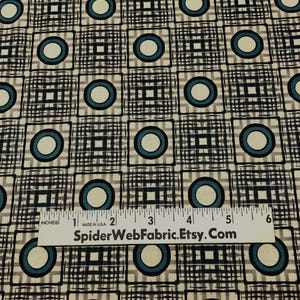May include: Fabric with a repeating pattern of teal circles within black squares and a cream background. The squares are set against a black and cream grid pattern. A ruler is placed on the fabric.