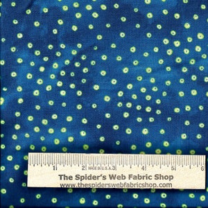 Op de afbeelding: Blauwe stof met een wit en groen stippenpatroon. De stof wordt gemeten met een liniaal waarop "The Spider's Web Fabric Shop" en "www.thespiderswebfabricshop.com" staat.