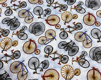 May include: A light blue fabric featuring a repeating pattern of vintage bicycles in red, gold, and black. A wooden ruler is positioned at the bottom, showing a scale of 6 inches for size reference.