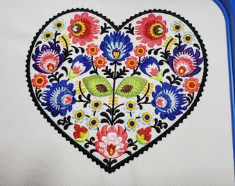 Peut inclure: Motif brodé en forme de cœur avec un motif d'art populaire traditionnel. Le motif présente une variété de fleurs colorées, de feuilles et de volutes dans des tons de rouge, bleu, vert, jaune et blanc.