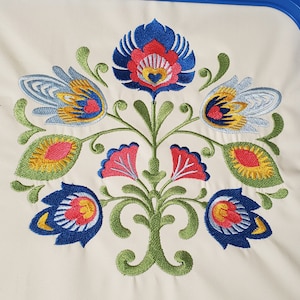 Op de afbeelding: Geborduurde bloemenmotief met blauwe, rode, gele en groene bloemen op een witte achtergrond.