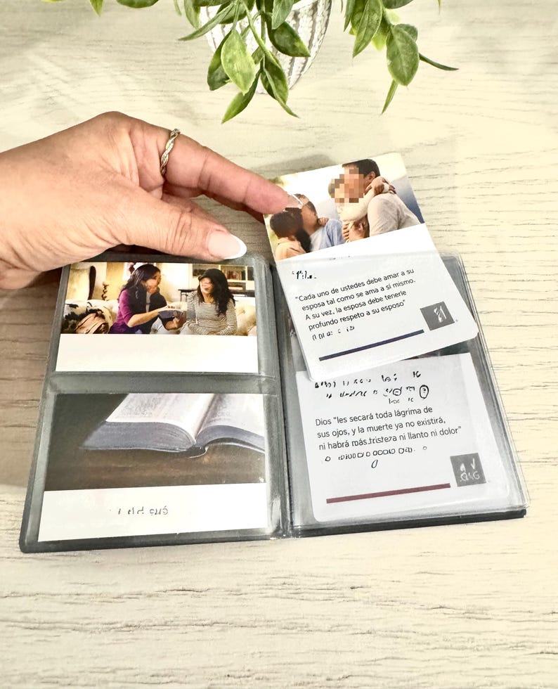 May include: A clear plastic photo album with several photos and text inserts. The album is open, displaying images of people and text in Spanish. The text includes phrases like "Cada uno de ustedes debe amar a su esposa" and "Dios les secar&aacute; toda l&aacute;grima".
