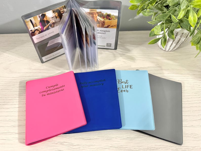 May include: A collection of colorful binders and clear plastic display cases. The binders are pink, blue, light blue, and gray, with text on the covers. The display cases hold printed cards with images and text.