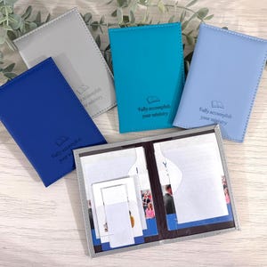 Peut inclure: Plusieurs porte-passeports en similicuir de couleurs bleu, turquoise, bleu clair et gris. Chaque étui porte un symbole de livre et le texte "Fully accomplish your ministry". Un étui est ouvert, révélant des poches intérieures.