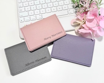 May include: Three personalised leather card holders in grey, pink and purple. The card holders have stitched edges and the names "Alberto Hussman", "Mary Martinez", and no name on the purple card holder are printed on the front.