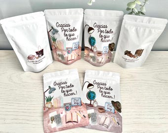 May include: White pouches with watercolor illustrations and the text "Gracias Por todo lo que hacen!" Each pouch features different illustrations, including a globe, books, a lamp, and a hat. The pouches are sealed and appear to contain a product.