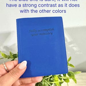 May include: A cobalt blue notebook with the text "Fully accomplish your ministry" is held in a hand. The notebook is surrounded by green foliage. The text "TAKE NOTE: The blue one is dark, It will not have a strong contrast as it does with the other colors" is at the top.