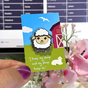 Puede incluir: Un pin de esmalte blanco con una oveja de dibujos animados y el texto "Conozco mis ovejas y mis ovejas me conocen". El pin está en una tarjeta con un granero de dibujos animados y un campo verde.