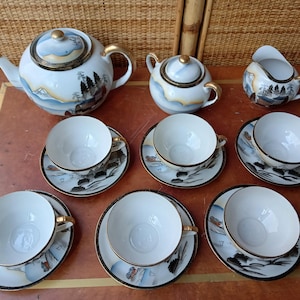 Op de afbeelding: Een wit theeservies met gouden accenten en een Japans geïnspireerd ontwerp. De set bevat een theepot, suikerpot, roomkan en zes theekopjes met schoteltjes.