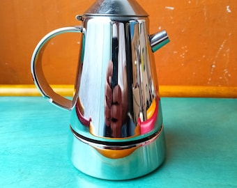 May include: A shiny, stainless steel stovetop espresso maker with a black knob on top. The coffee pot has a handle and a spout. The polished surface reflects the surrounding colors of orange and teal.