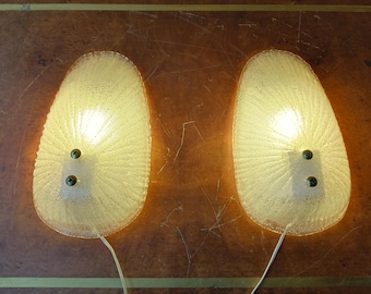 May include: Two white glass wall sconces with a textured, fan-like design. Each sconce has two small, green screws and a light bulb turned on.