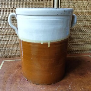 May include: A large, cylindrical ceramic pot with a two-tone design. The upper portion is white, while the lower section is a warm brown. It features two curved handles and a slightly flared rim. The pot is approximately 46 cm tall.