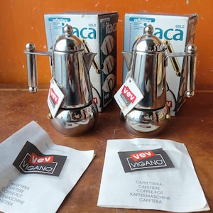 Puede incluir: Dos cafeteras italianas Vev Vigano Itaca de acero inoxidable pulido con base redondeada, mango cilíndrico y tapa abovedada. Cada unidad incluye su caja de embalaje de cartón original y un manual de instrucciones blanco con el logotipo de Vev Vigano.