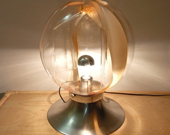 May include: A modern table lamp with a clear glass globe shade featuring a swirling, amber-colored design. The lamp has a silver metal base.