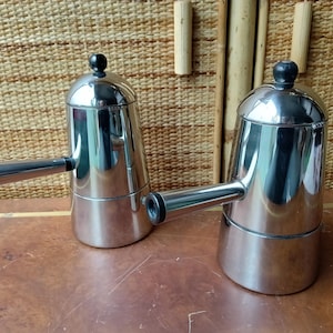 May include: Two silver stovetop espresso makers with black handles. The espresso makers are made of stainless steel and have a polished finish.