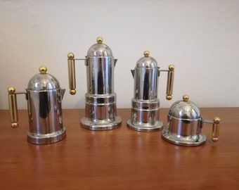 May include: Four silver and gold coffee makers of different sizes. The coffee makers have a rounded top and a handle with a gold knob.