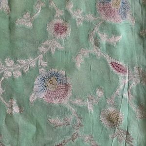 May include: A light mint green fabric featuring an intricate woven floral pattern. The design includes stylized flowers in shades of soft pink, blue, and metallic silver, connected by delicate, winding leafy vines across the entire surface.
