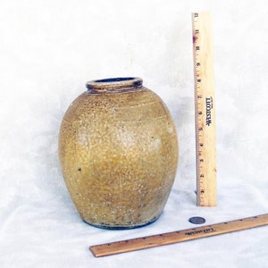 May include: A large, round, yellow ceramic jar with a textured surface. The jar is about 10 inches tall and 7 inches wide. It is sitting on a white surface.