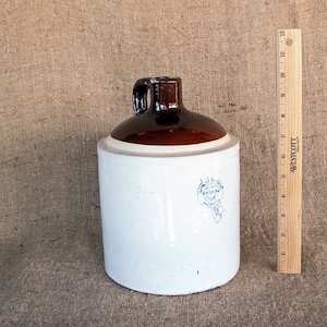 May include: A white and brown ceramic jug with a brown handle and a blue and white logo that says "Blue Ribbon" on the front. The jug is sitting on a burlap background.