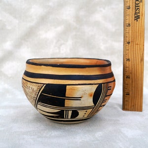 May include: A small, hand-painted pottery bowl with a black and white geometric design on a tan background. The bowl is about 3 inches tall and 4 inches wide.
