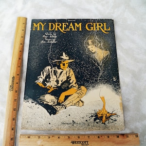May include: A vintage sheet music cover for the song "My Dream Girl" by Ray White and Jim Schiller. The cover features a black and white illustration of a man sitting by a campfire with a woman's ghostly image appearing above him.