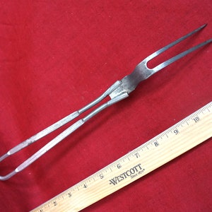 May include: A silver metal grilling fork with a long handle and two prongs. The fork is about 12 inches long and has a loop at the end of the handle.