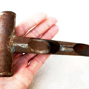 May include: A rusty metal tool with a T-shaped handle and a long, narrow scoop. The tool is designed for planting seeds or bulbs.