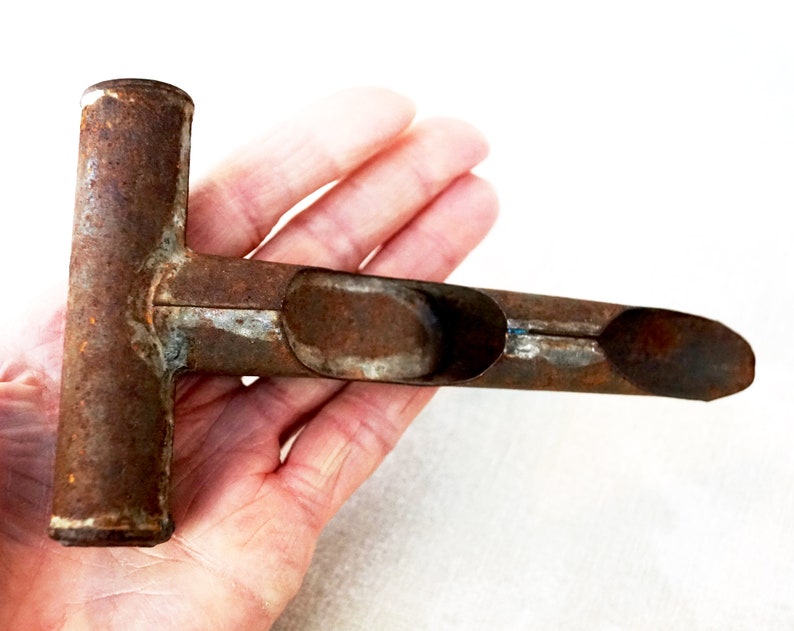 May include: A rusty metal tool with a T-shaped handle and a long, narrow scoop. The tool is designed for planting seeds or bulbs.
