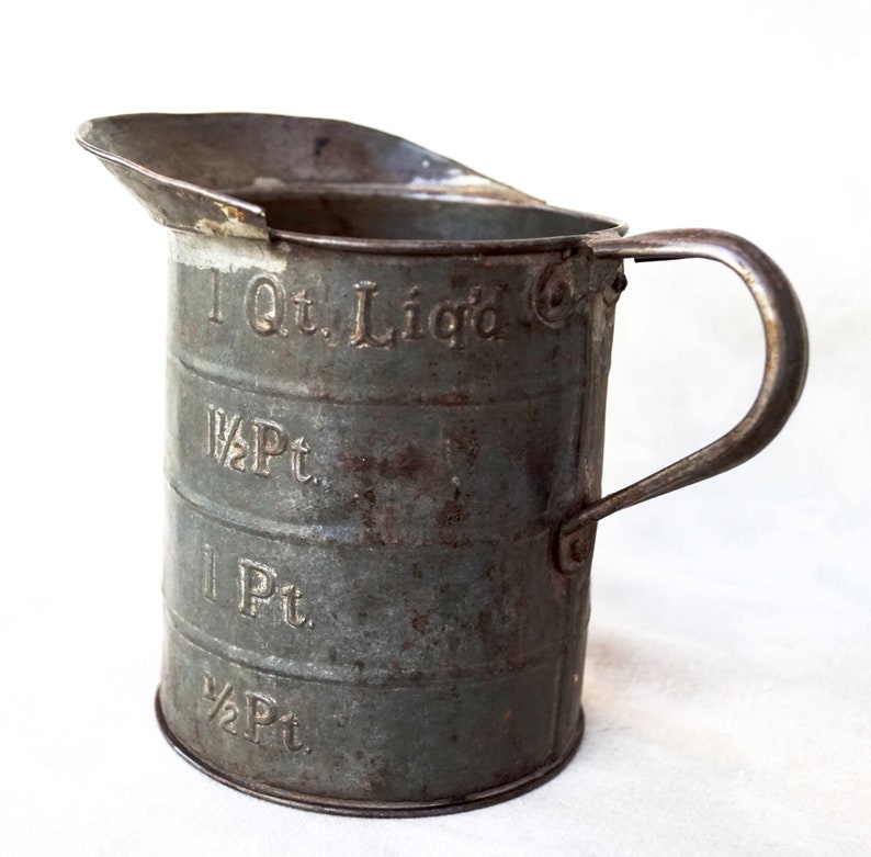 May include: A vintage metal measuring cup with a handle. The cup is marked with measurements in quarts and pints: 1 Qt. Liq'd, 1 1/2 Pt, 1 Pt, 1/2 Pt.